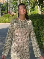 Woman wearing a patterned dress standing outdoors with greenery in the background