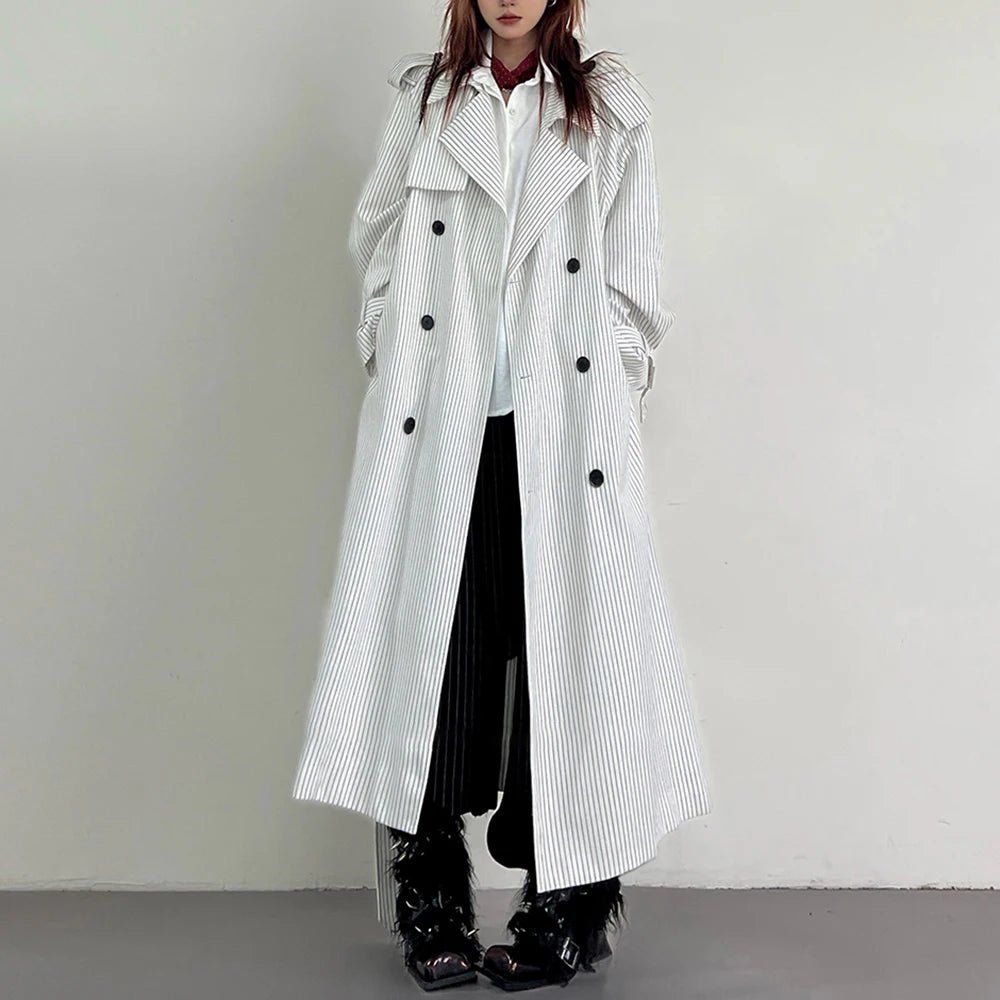 Person wearing a long white coat with black buttons on a plain background