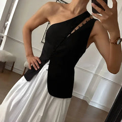 Person wearing a black one-shoulder outfit with white pants, taking a mirror selfie.