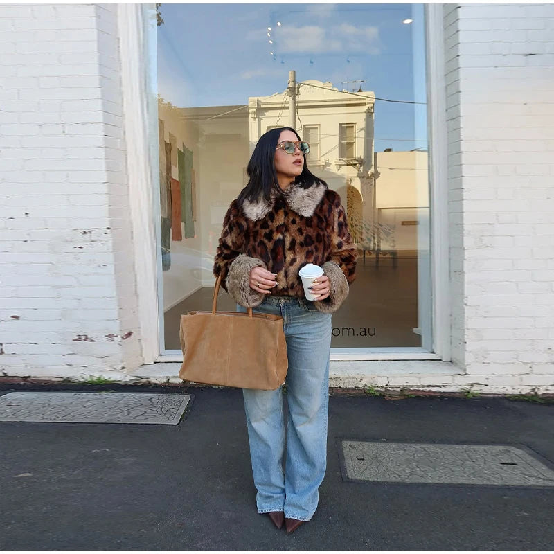 Woman in a leopard print coat holding a coffee cup and a brown bag, standing in front of a store window.