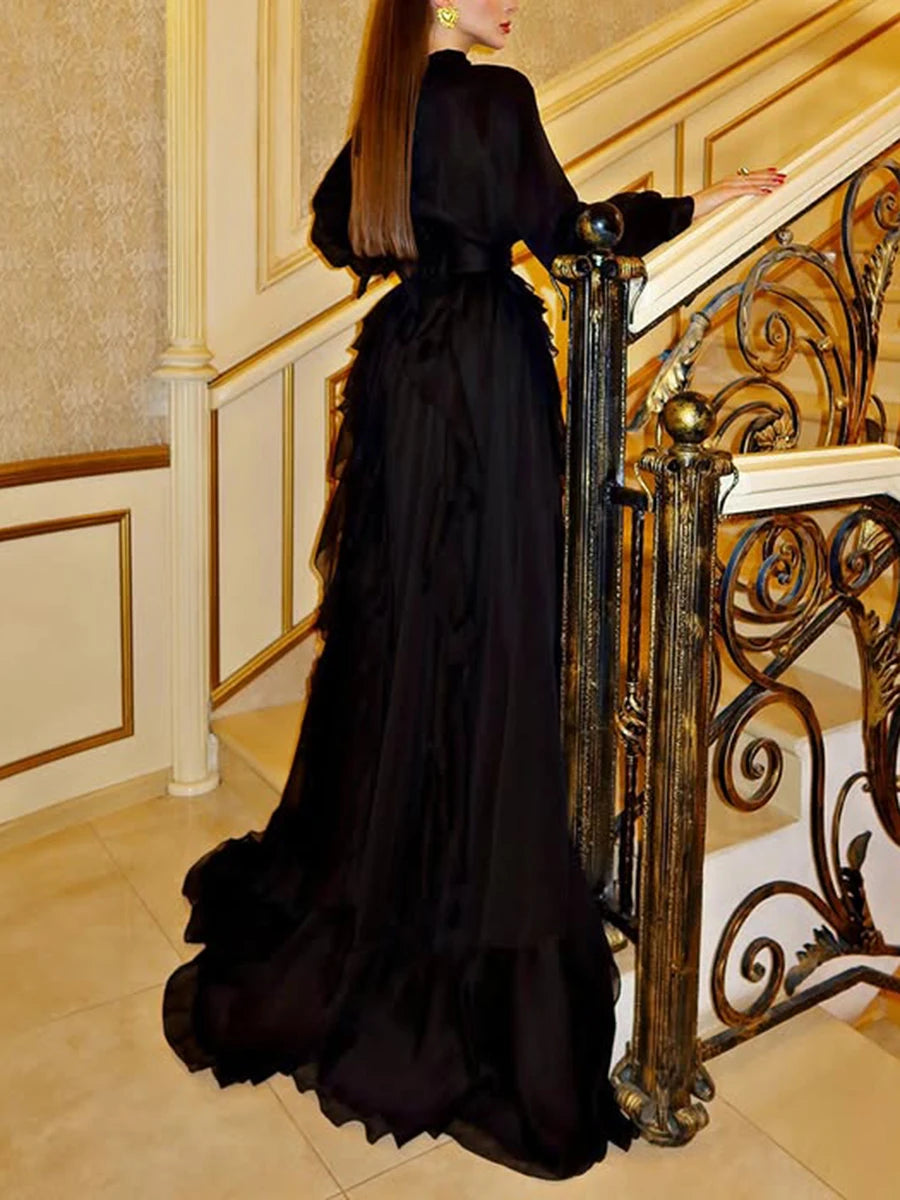 Woman in a black evening gown standing on a staircase with ornate railings.
