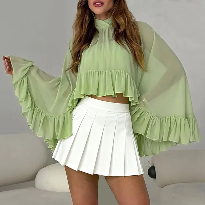 Woman wearing a light green blouse with ruffled sleeves and a white pleated skirt.