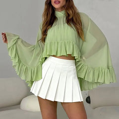 Woman wearing a light green blouse with ruffled sleeves and a white pleated skirt.