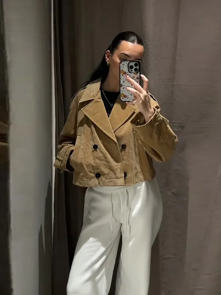 Person wearing a tan jacket and white pants taking a mirror selfie.