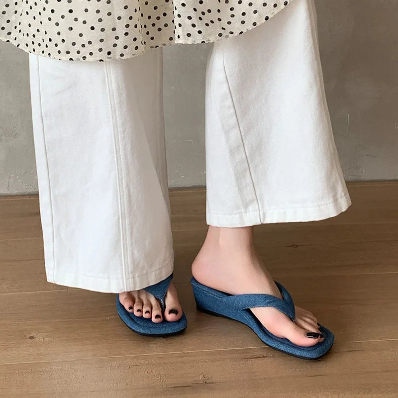 Blue denim wedge flip flops on feet