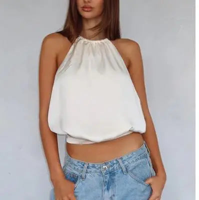 Woman wearing a white halter top and blue jeans against a plain background