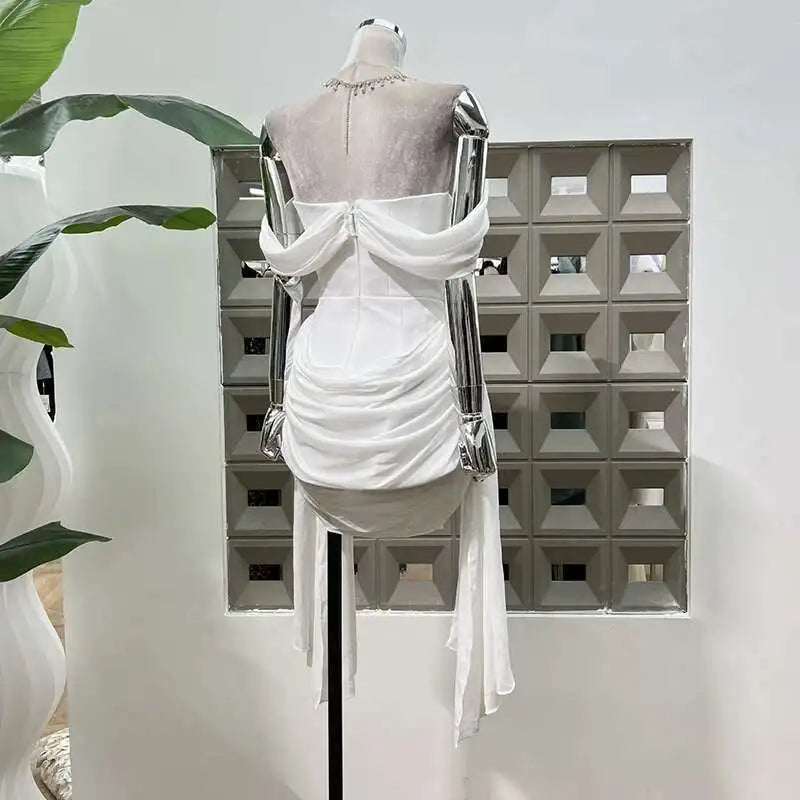 White dress on a mannequin against a geometric wall with plants.