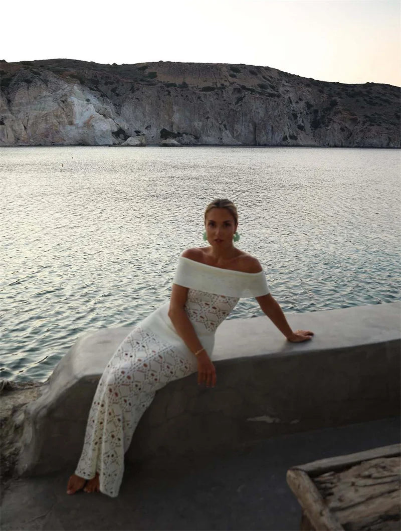 Woman in a white dress sitting by a body of water with cliffs in the background