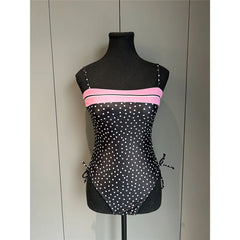 Black mannequin displaying a black and white polka dot one-piece swimsuit with pink stripe and adjustable side ties.