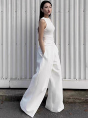 Woman wearing a white sleeveless jumpsuit against a white wall.