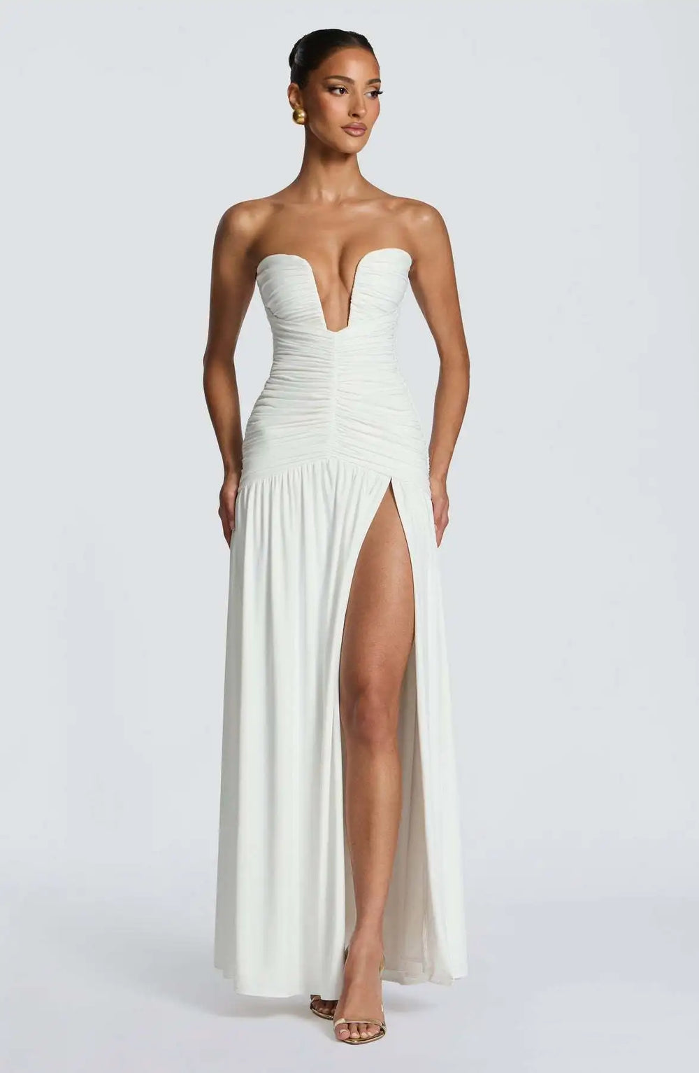 Woman wearing a white strapless gown with a high slit on a white background