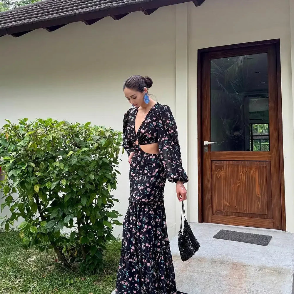 Woman in a floral dress standing outside a house with a wooden door.