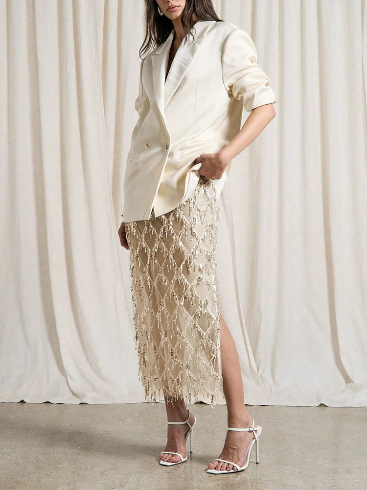 Woman wearing a cream blazer and lace skirt against a white curtain background