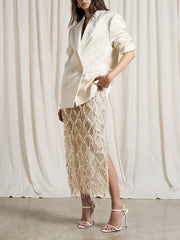 Woman wearing a cream blazer and lace skirt against a white curtain background
