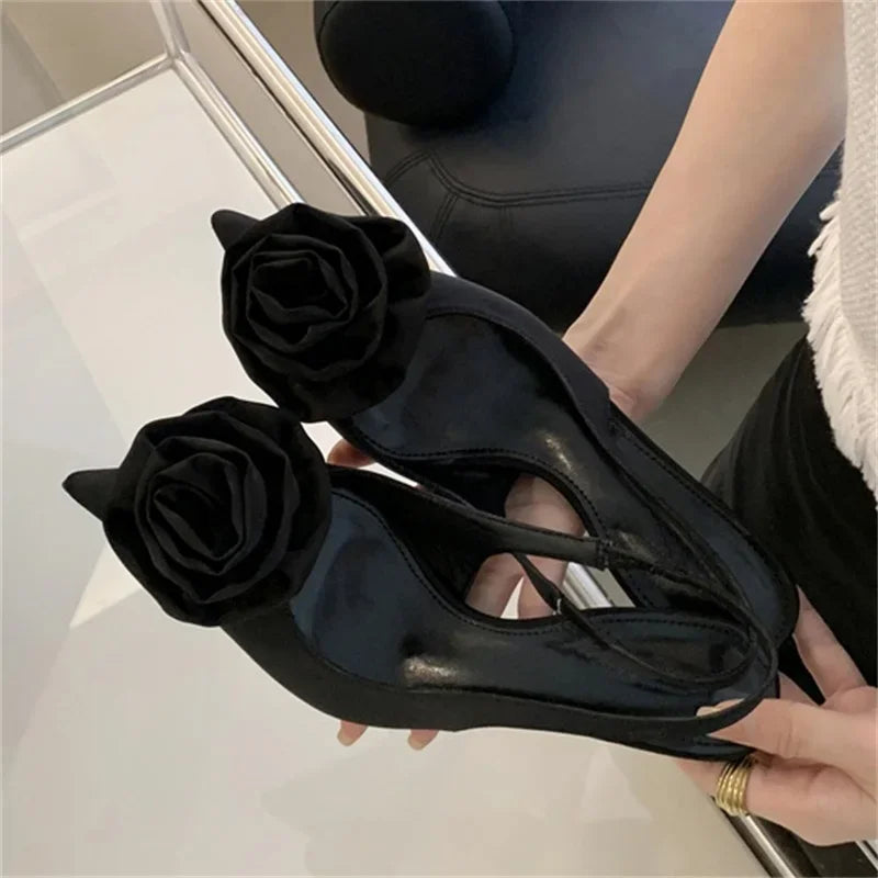 Black high-heeled shoes with floral decorations held by a person.