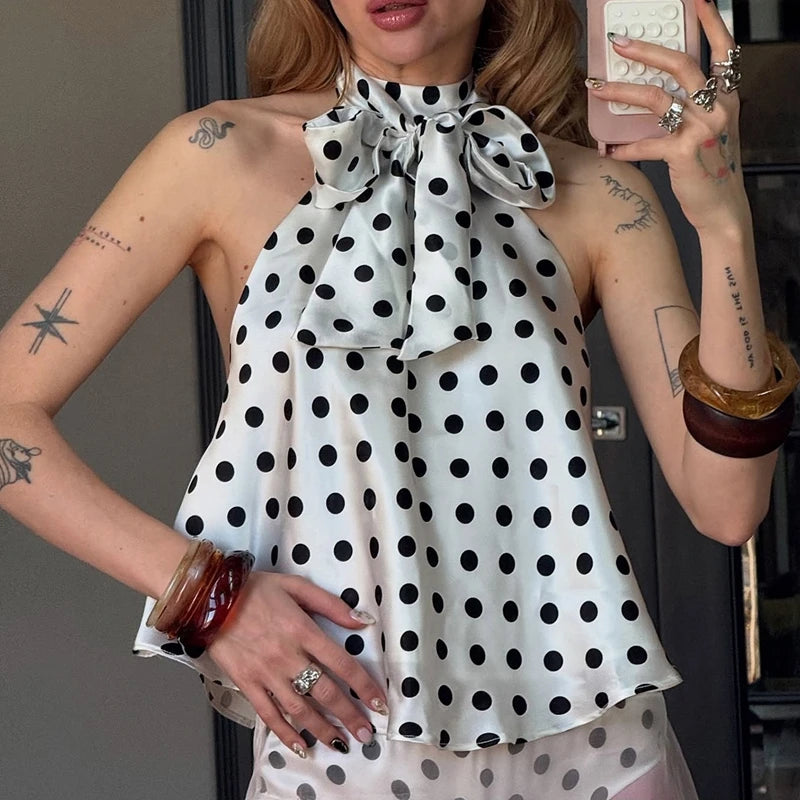 Woman wearing a polka dot dress with a large bow, taking a mirror selfie.