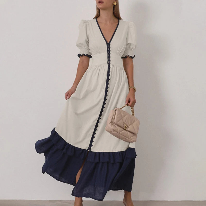 Woman wearing a white and navy dress holding a pink handbag against a plain background