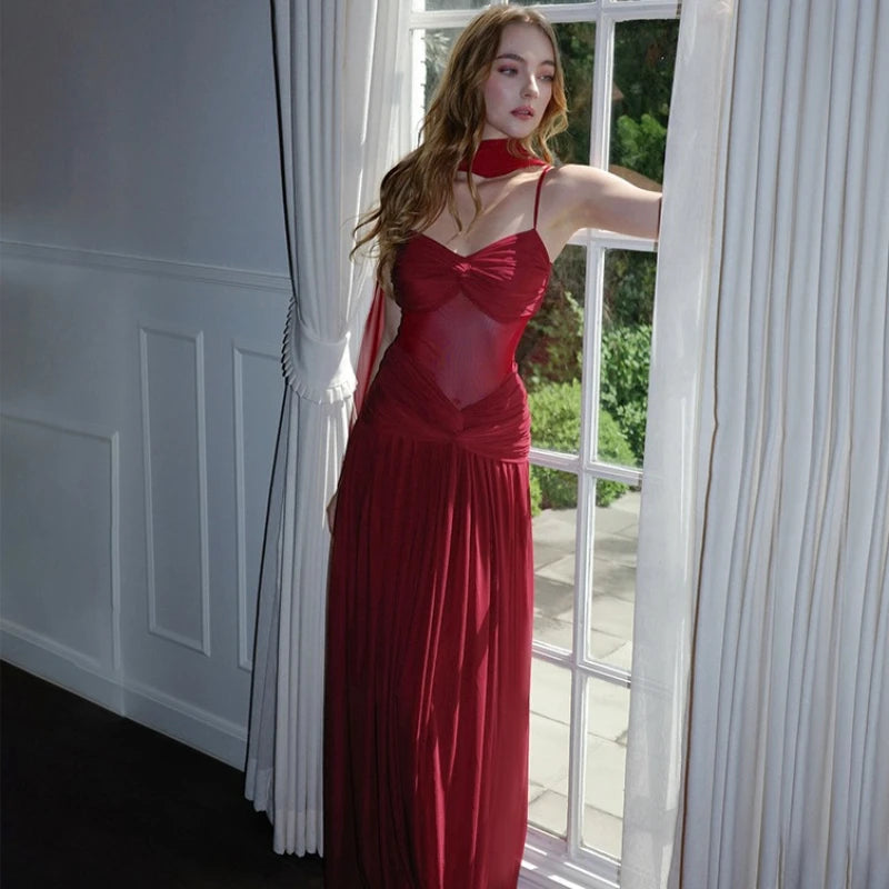 Woman in a red dress standing by a window with white curtains.