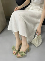 Model wearing light green heeled slides with a white dress