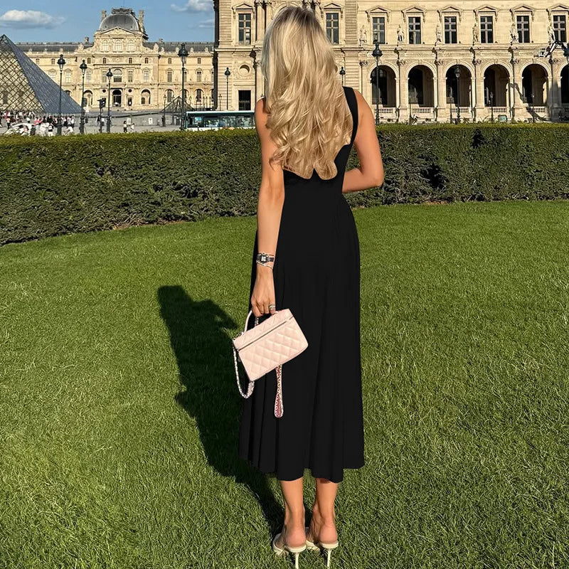 Woman in a black dress holding a pink handbag on grass with a historic building in the background