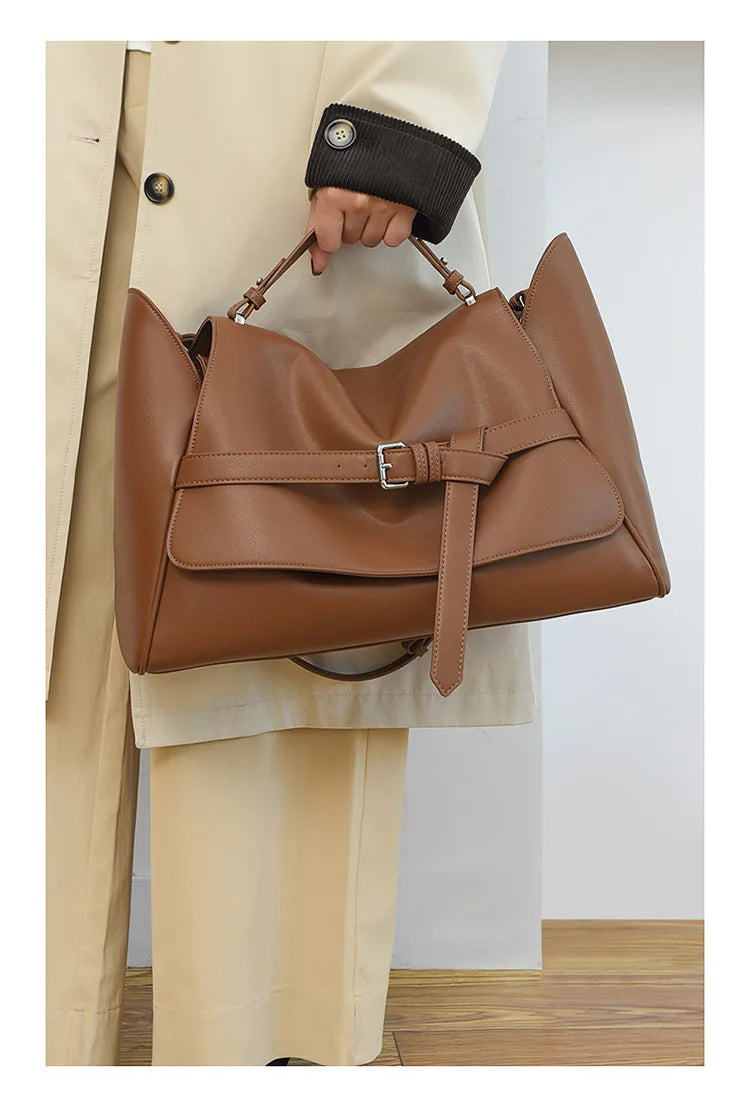 Brown leather handbag held by a person wearing a beige coat.
