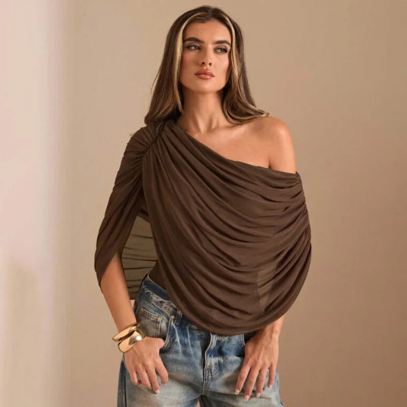 Woman wearing a brown one-shoulder top and blue jeans against a beige background
