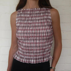 Person wearing a plaid sleeveless top against a white brick wall.