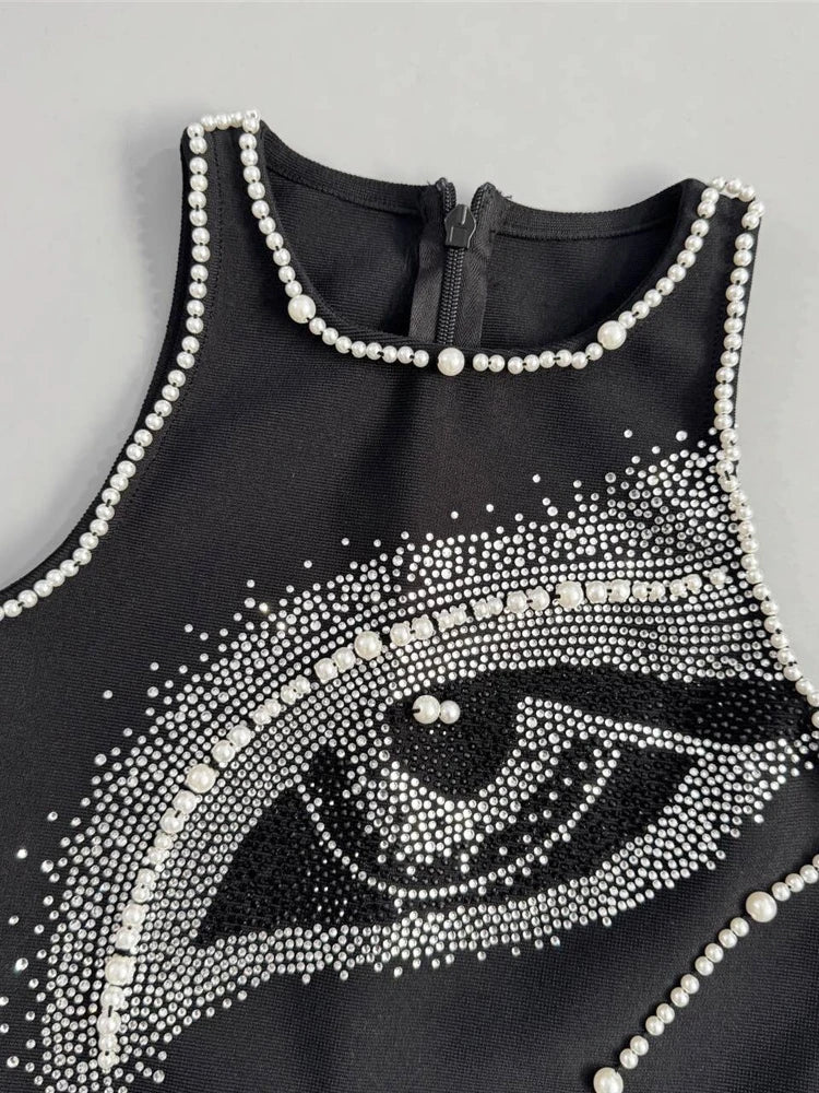 Black sleeveless top with eye design and pearl embellishments on a gray background