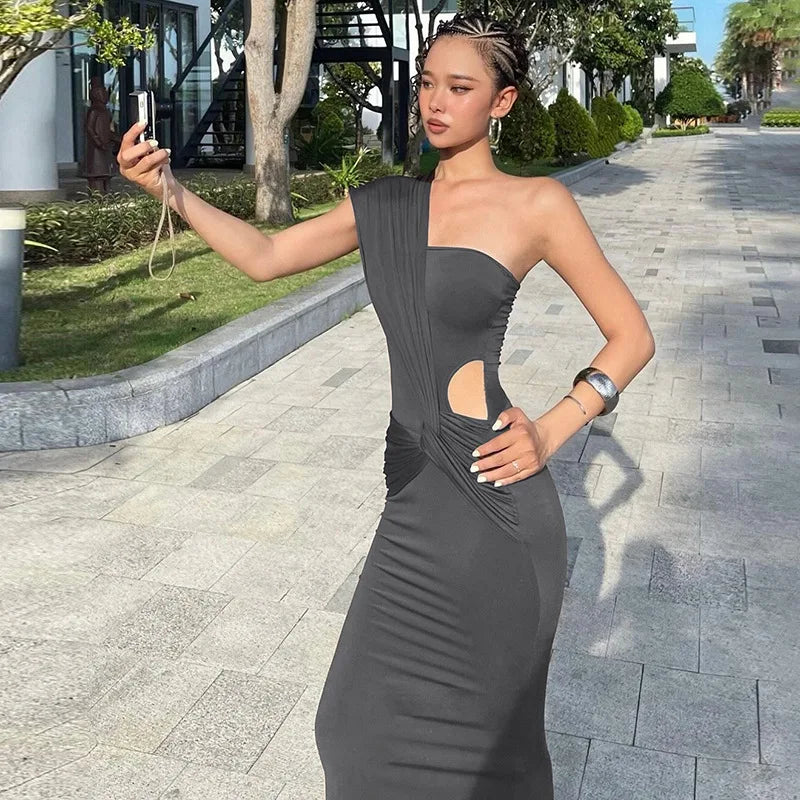 Woman in a gray one-shoulder dress taking a selfie on a sidewalk.