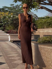 Woman in a brown dress standing outdoors near a pool with greenery in the background