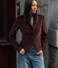 Woman wearing a brown blazer and blue jeans standing against a stone wall.