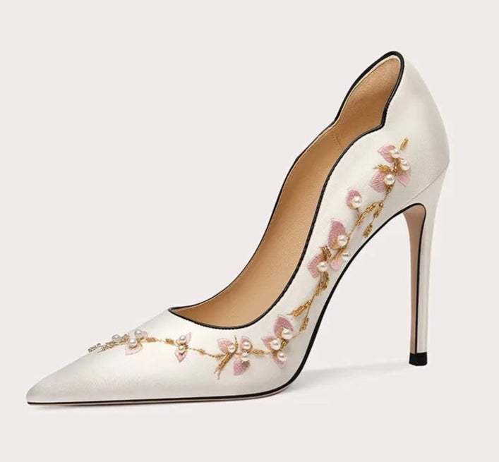 White high-heeled shoe with floral embroidery on a light gray background