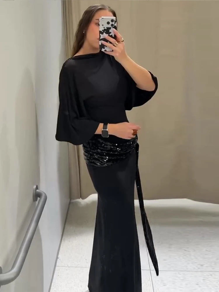 Woman taking a mirror selfie wearing a black outfit with a slit skirt.
