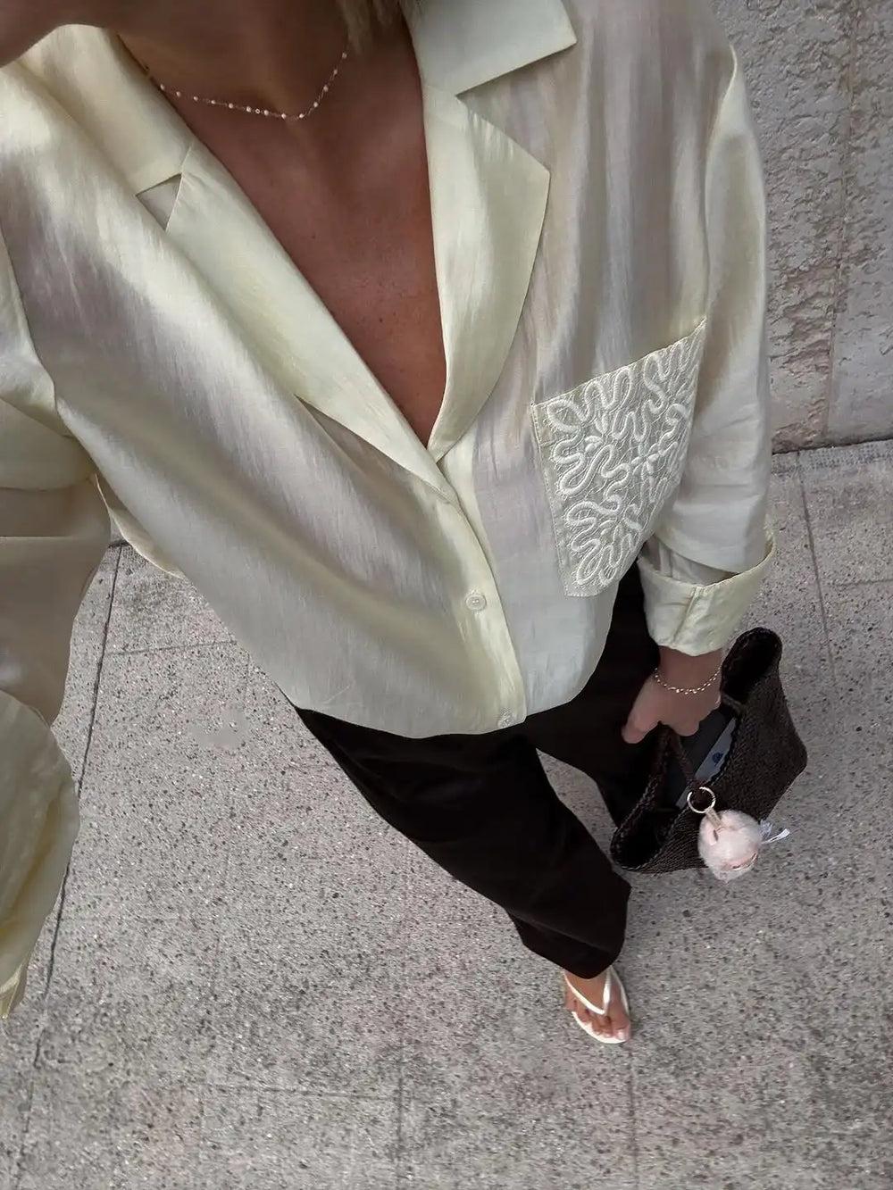 Person wearing a light-colored blouse with a decorative pattern on a pavement background