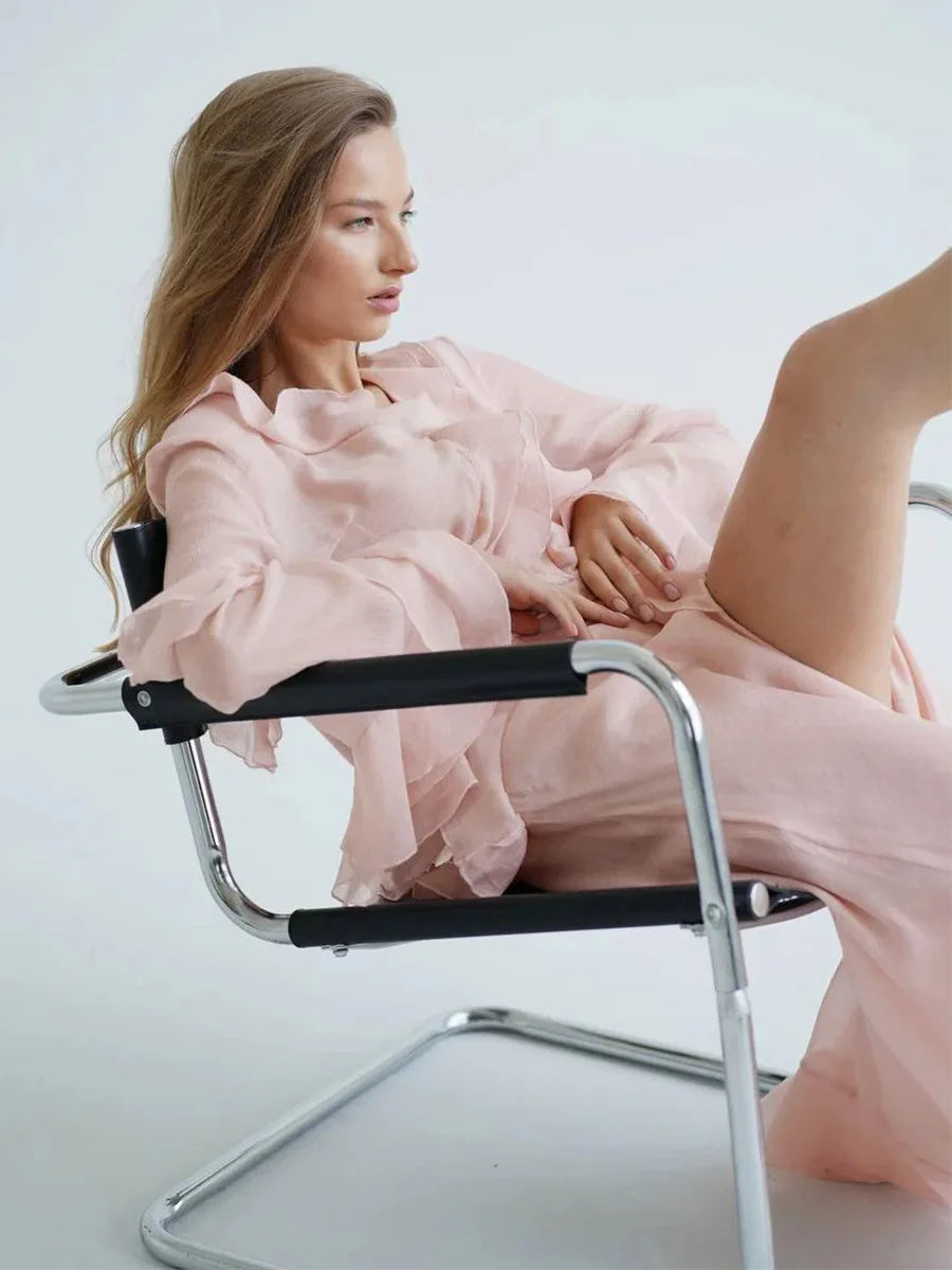 Woman in a pink dress sitting on a modern chair against a white background