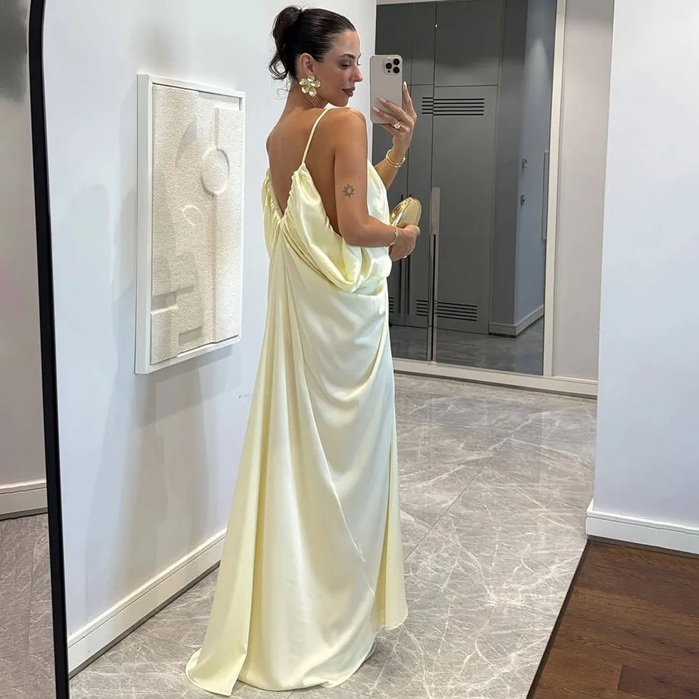 Woman in a light yellow satin dress taking a mirror selfie in an indoor setting.