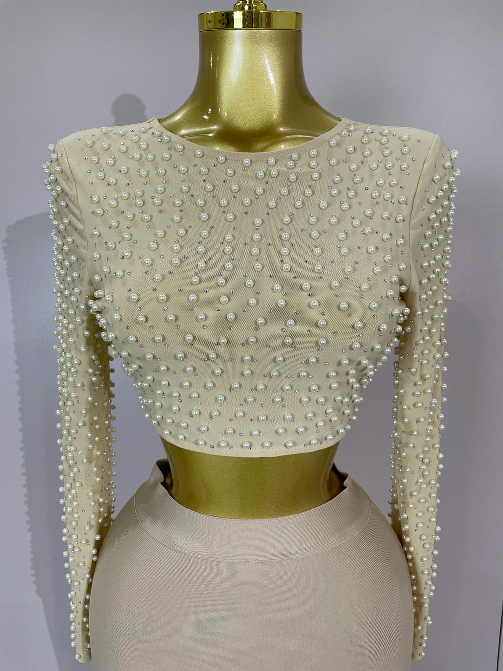 Mannequin wearing a beige top with pearl embellishments on a gray background