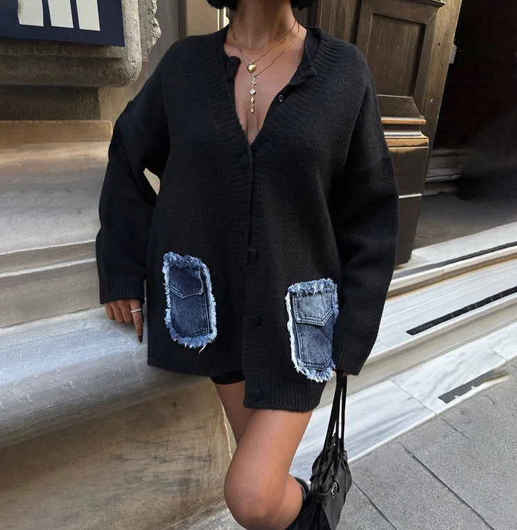 Person wearing a black cardigan with denim pocket patches on a city street.