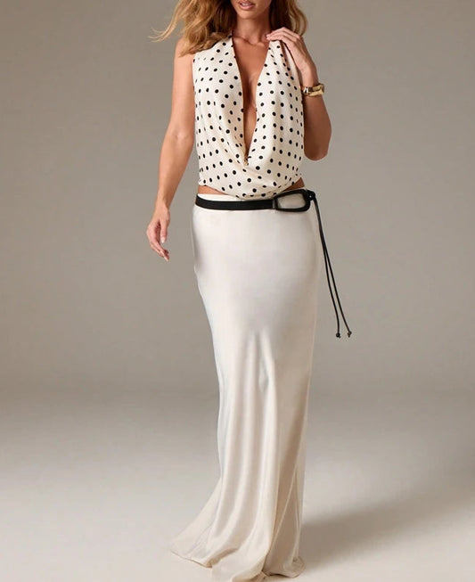 Woman wearing a polka dot top and white skirt with a belt on a plain background