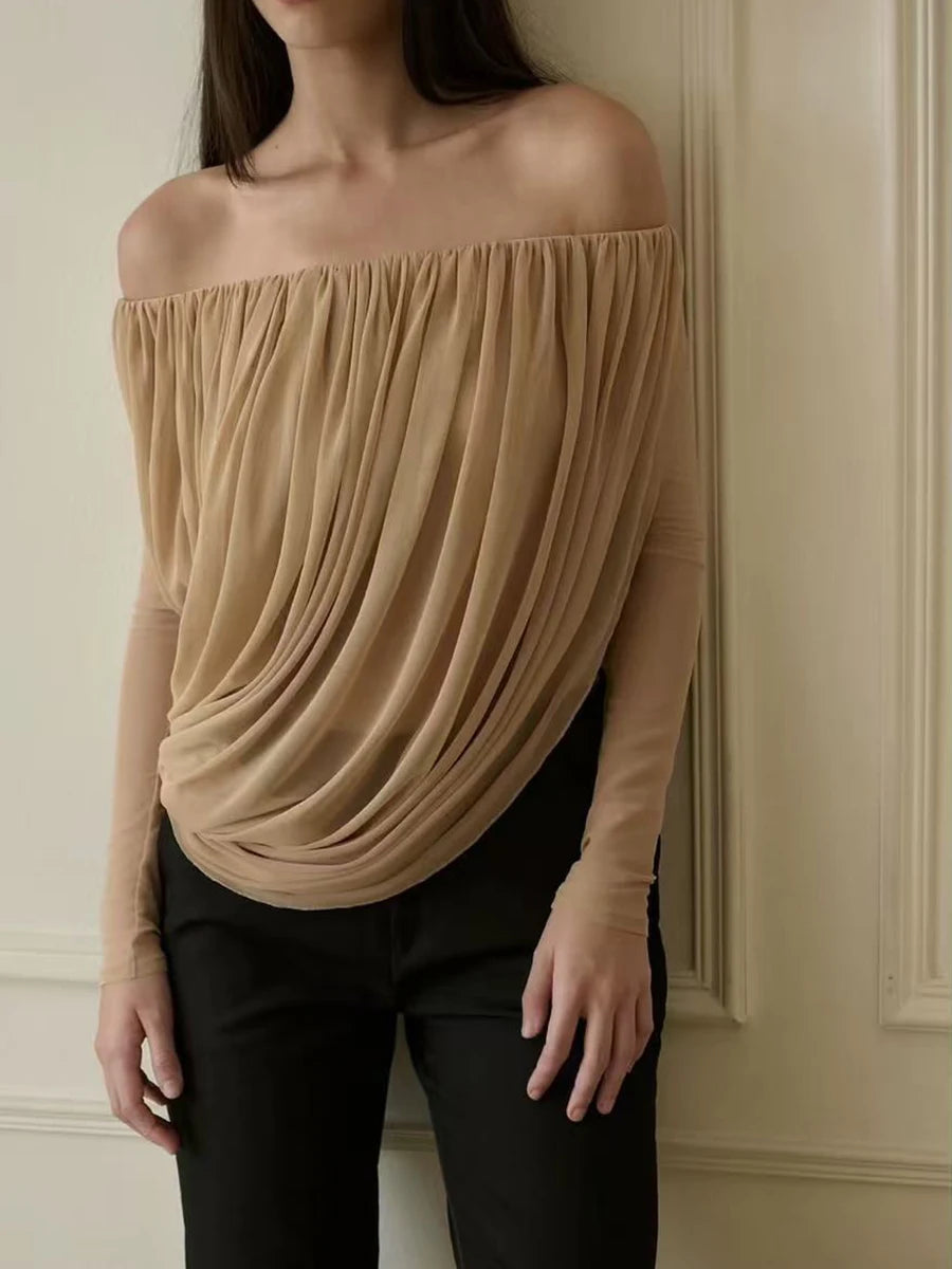 Woman wearing a beige off-shoulder top against a neutral wall.