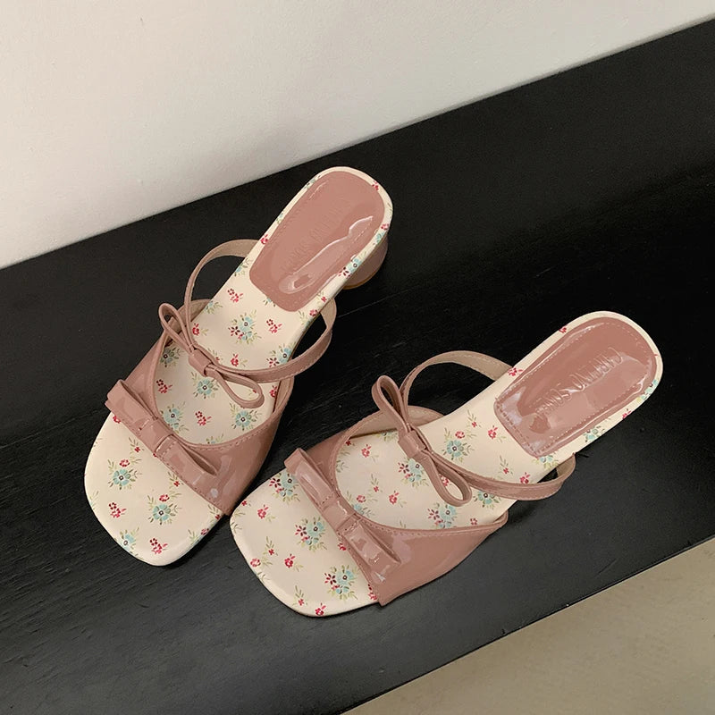 Pair of pink floral sandals on a black surface with a white background