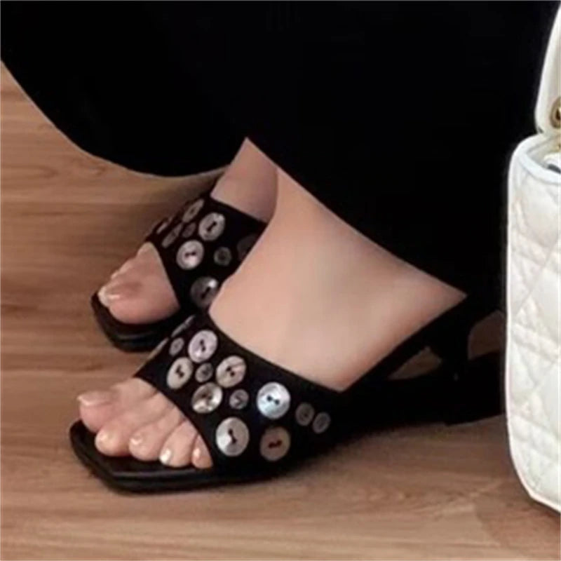 Foot wearing a black square toe mule sandal with shell buttons
