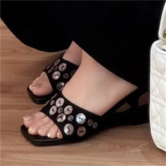 Foot wearing a black square toe mule sandal with shell buttons