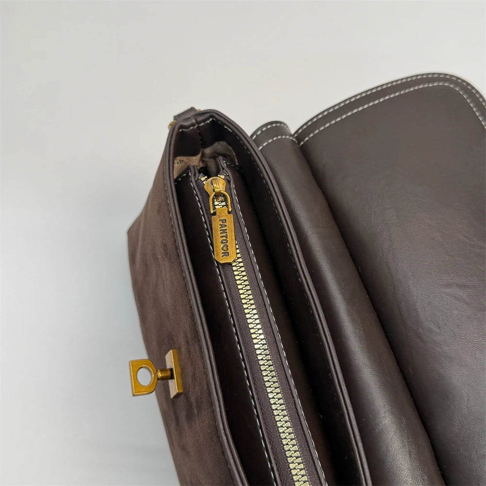 Brown leather clutch bag with gold zipper and clasp on a light gray background