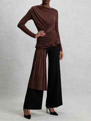 Woman wearing a brown top and black pants on a light gray background