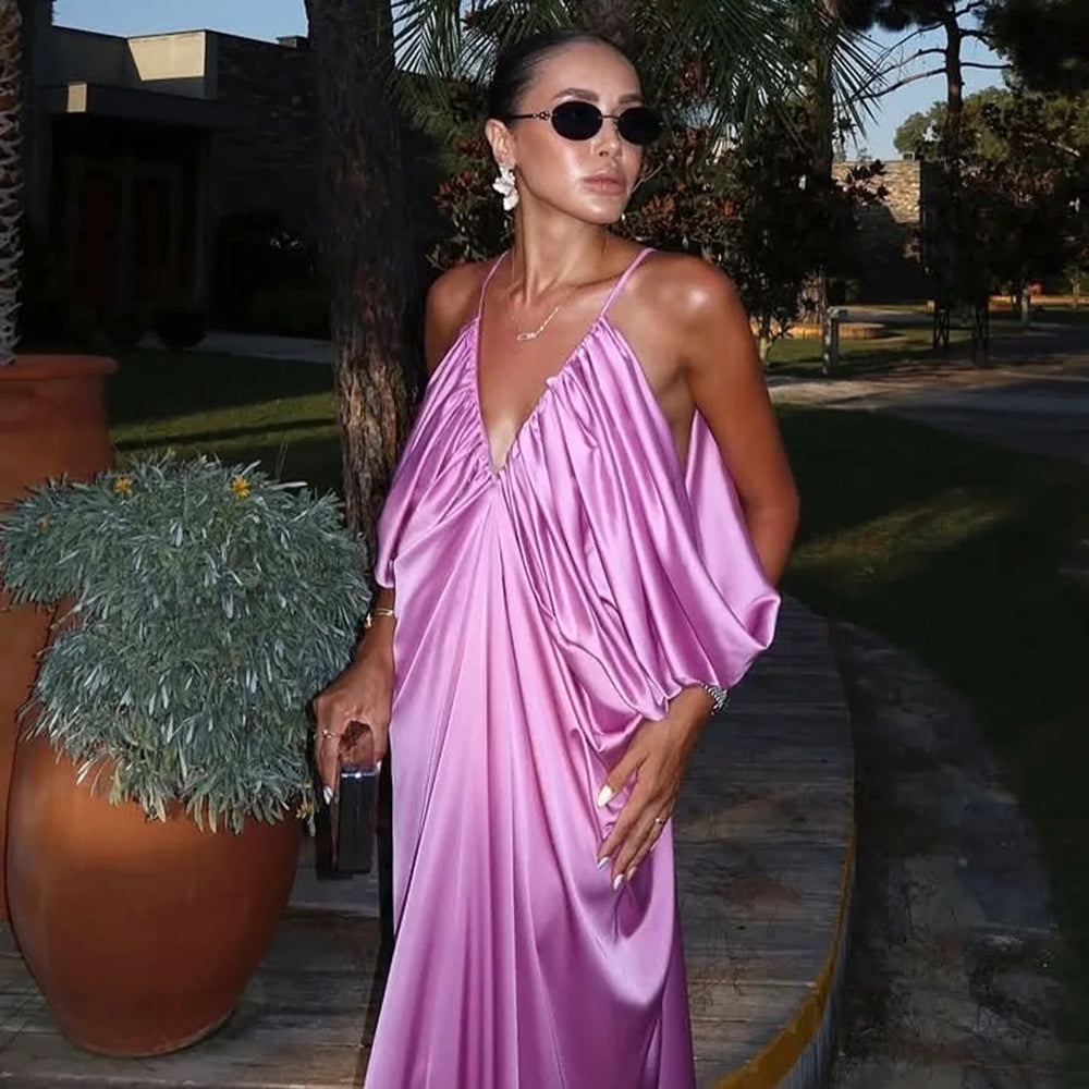 Woman in a pink dress standing outdoors with plants and a building in the background