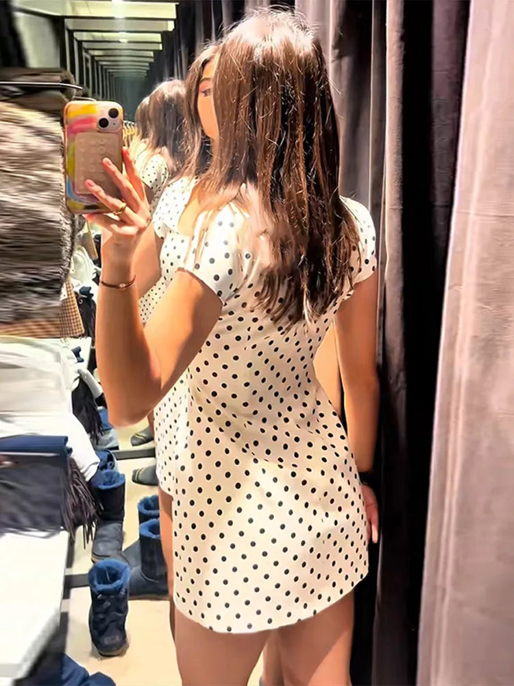 Person taking a mirror selfie wearing a polka dot dress in a clothing store.