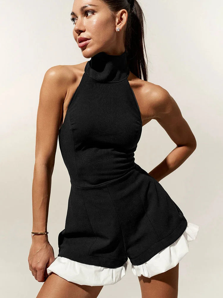 Woman wearing a black halter neck and white romper against a plain background