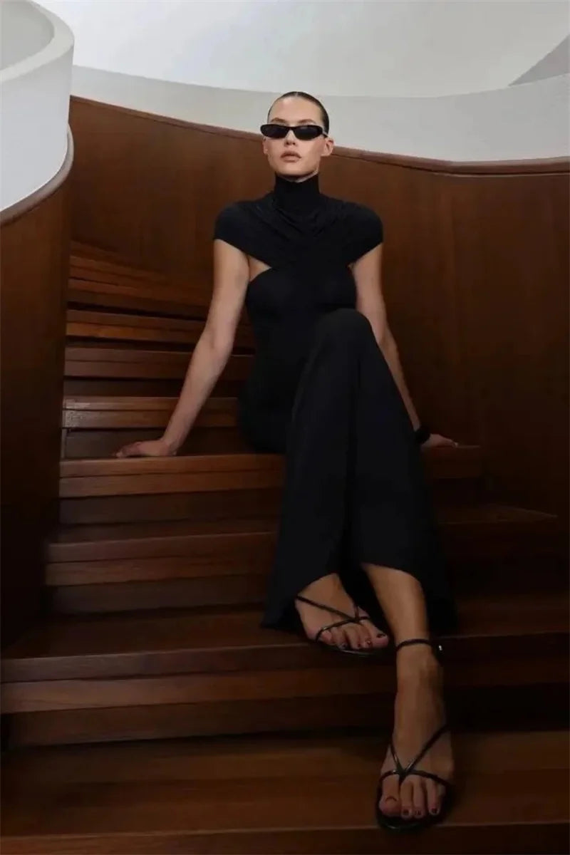 Woman in a black dress sitting on wooden stairs wearing sunglasses.