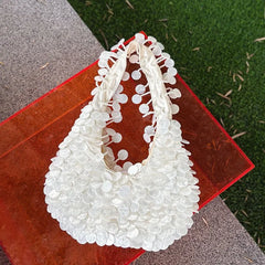 White beaded handbag on a red surface with grass in the background